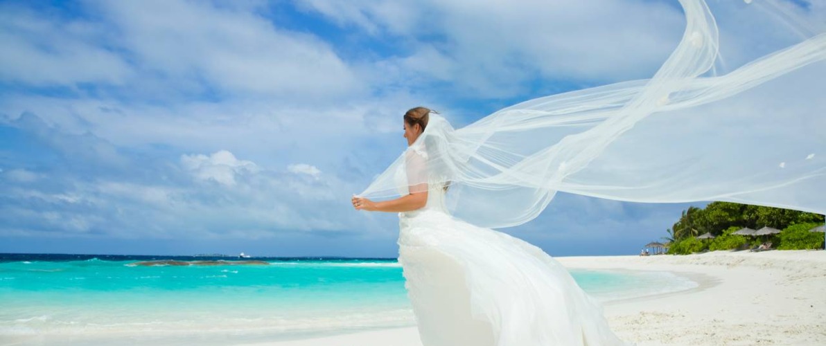 White wedding dress with big long white veil stand on shore sea